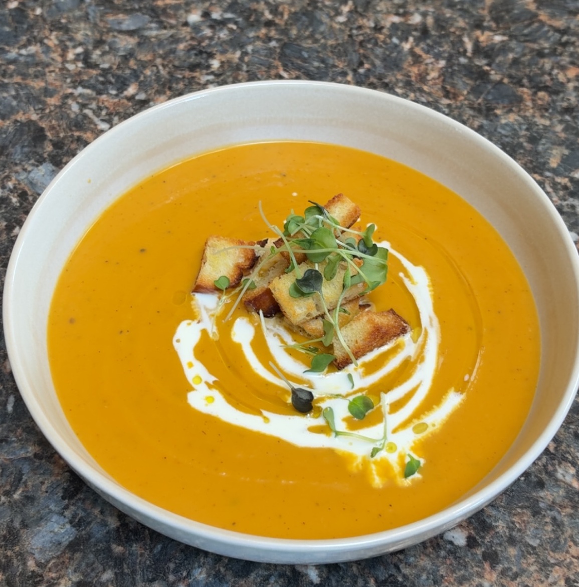 Homemade roasted butternut squash soup with cream, croutons and microgreens